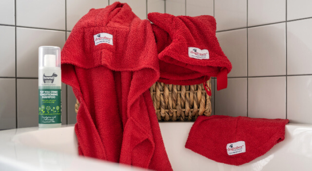 Red dog dressing gown, dog Snood and dog drying mitts by Dogrobes UK ready to be used on side of bath with Hownd Shampoo.