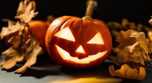 Lit pumpkin with smiling face lying among dried autumn leaves